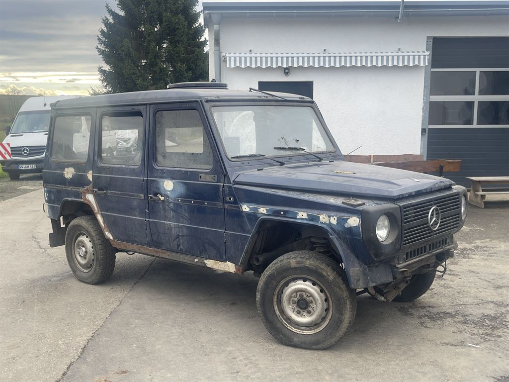 Der dunkelblaue Mercedes G von schräg vorn, vollständig, mit sichtbarem Rost an Schwellern, Radläufen und Kotflügeln.